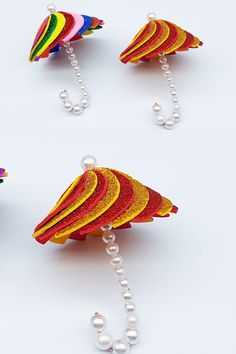 three colorful objects are hanging from chains on a white surface, with pearls attached to them