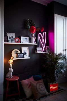 a living room with black walls and pink neon lights on the shelves above it is decorated with various items