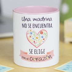 a pink and white coffee mug sitting on top of a wooden table next to two cards