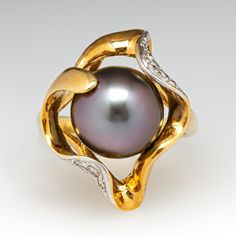 This captivating ring features an organic design and is centered with one (1), post set, cultured Tahitian pearl. The pearl is bordered with eight (8), bead set, round brilliant cut diamonds. The ring measures 22.7mm at the top, rises 12.8mm above the finger, tapering to 2.6mm wide and 0.9mm thick at the base of the shank. This ring is currently a size 7.75. Elegant Yellow Gold Tahitian Pearl Rings, Formal Yellow Gold Tahitian Pearl Ring, Classic Tahitian Pearl Ring With Diamond Accents, Tahitian Pearl Ring With Diamond Accents Fine Jewelry, Fine Jewelry Tahitian Pearl Ring With Diamond Accents, Elegant Tahitian Pearl Ring With Diamond Accents, Tahitian Pearl Ring With Diamond Accents, Formal Tahitian Pearl Ring With Diamond Accents, Diamond Cocktail Ring