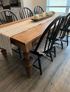 a wooden table with black chairs and a bowl of food on it's end