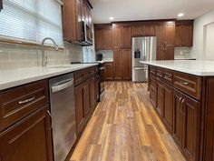 an empty kitchen with wooden floors and stainless steel appliances in the center, along with white counter tops