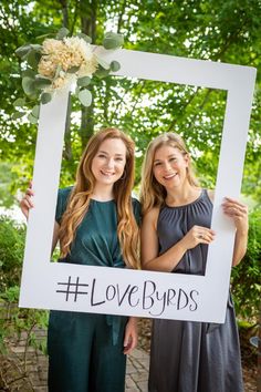 two girls holding up a sign with the words lovebirds written on it in front of them