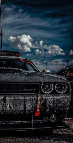 a black car parked in a parking lot next to other cars with clouds in the background