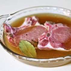 two raw meats in a bowl with sauce and leaves on the side, ready to be eaten