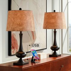 two lamps sitting on top of a wooden dresser next to a mirror and phone charger