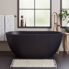 a black bath tub sitting next to a window in a bathroom with a rug on the floor