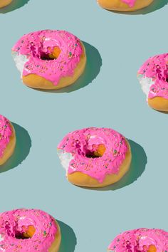 several donuts with pink frosting and sprinkles are arranged on a blue background