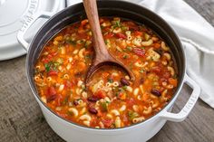 a pot filled with pasta and vegetables on top of a wooden table next to a white plate