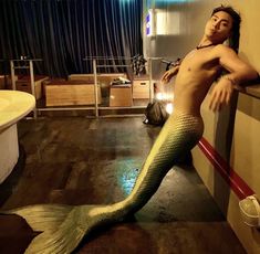 a man with no shirt on standing next to a mermaid tail