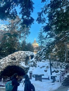 two people walking in the snow towards a stone arch with a domed building on top