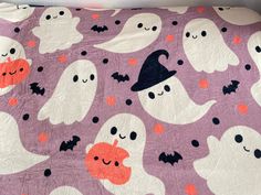 a bed covered in purple and white ghost quilts with orange pumpkins on them