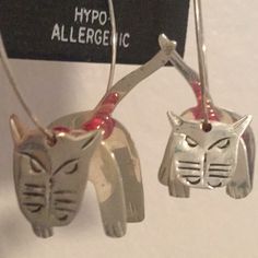 two silver cat earrings hanging from hooks on a white surface with a sign that says hypo allergenic