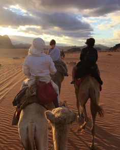 three people riding camels in the desert at sunset with other people walking behind them