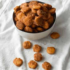 a bowl filled with fried food sitting on top of a white cloth next to a pile of doughnuts