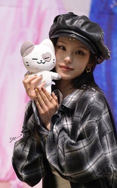 a woman holding a white cat doll in her hands and wearing a black hat on top of her head