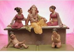 three small statues of women sitting on top of a bench with one baby in the middle