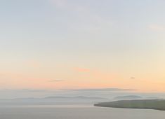 two cows grazing on the side of a large body of water with hills in the background