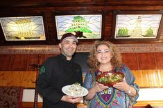 a man and woman holding plates of food in front of stained glass windows at a restaurant