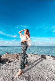 a woman standing on top of a rock next to the ocean with her arms behind her head