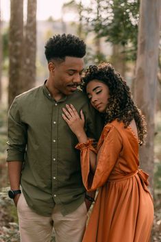 a man and woman standing next to each other in front of trees with their arms around each other