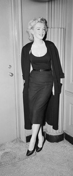 a woman standing in front of a door wearing a black dress and coat