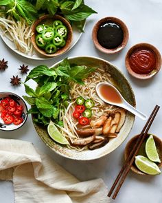 two bowls filled with noodles and vegetables next to dipping sauces