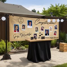 a table with pictures on it in the middle of a yard area, surrounded by trees and bushes