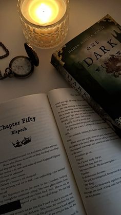 an open book sitting on top of a table next to a candle and pocket watch