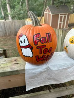 two pumpkins sitting on top of a wooden table in front of a fence with the words fall too vein painted on them