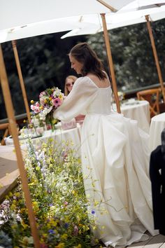 a woman in a white dress standing next to flowers and an umbrella over her head