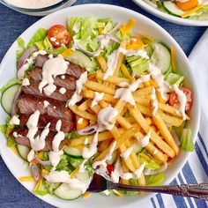 a salad with fries and dressing on the side next to a bowl of ranch dressing