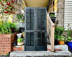 an open black door sitting on the side of a building next to potted plants