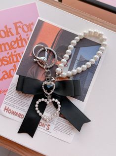 a key chain with pearls and a black bow on it sitting next to a book