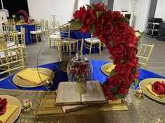 the table is set with red roses and gold place settings