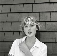 black and white photograph of a woman standing in front of a house with her hands on her chest