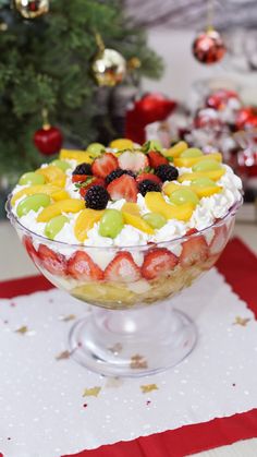 a dessert with fruit and whipped cream in a glass dish on a table next to a christmas tree