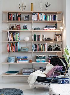 a living room filled with furniture and bookshelves next to a wall mounted lamp