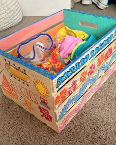 a wooden box filled with lots of colorful items on the floor next to a pile of shoes