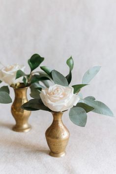 two gold vases with flowers in them on a table