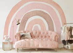 a pink couch sitting in front of a wall with a rainbow painted on it's side