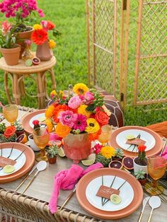 an outdoor table set with plates and flowers