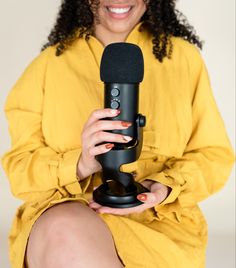 a woman is holding a microphone in her hands and smiling at the camera while sitting down