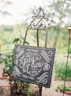 a sign that is on top of a metal stand in front of some plants and trees