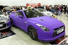 two purple sports cars parked next to each other in a showroom filled with people