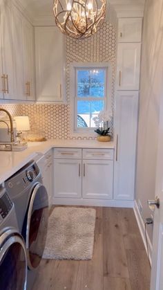 a washer and dryer in a small room with white cabinets, wood flooring and a chandelier