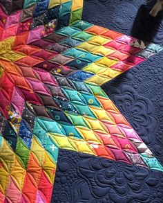 a colorful quilt is laying on top of a blue table cloth with an animal standing next to it