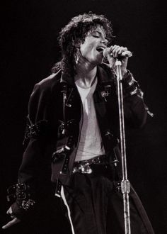 michael jackson performing on stage with microphone in his hand and wearing black leather pants, white t - shirt and jacket