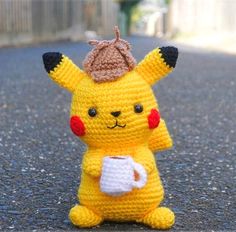 a small crocheted pikachu holding a coffee cup in its hand on the street