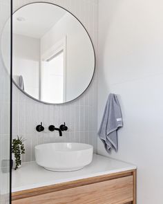 a white sink sitting under a round mirror